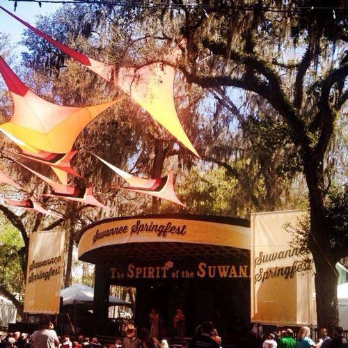 Outdoor festival entrance with colorful hanging sails and a sign reading “The Spirit of the Suwannee”