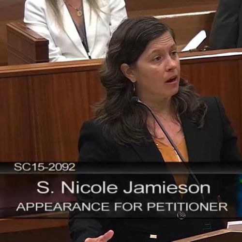 Attorney S. Nicole Jamieson speaking in a courtroom, wearing a black blazer over an orange top.