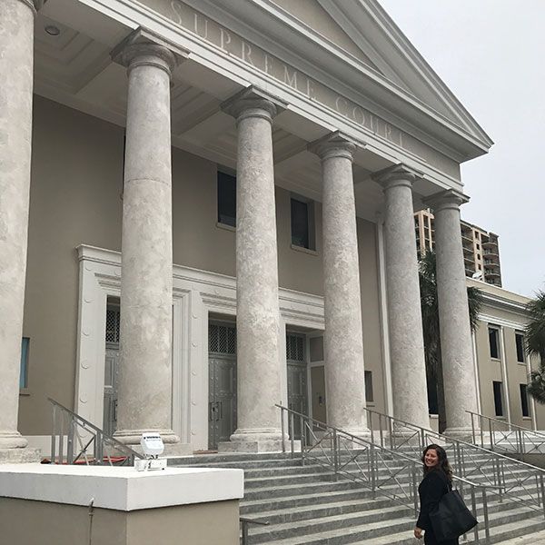 Large neoclassical building with tall columns and steps, with a person walking in front.
