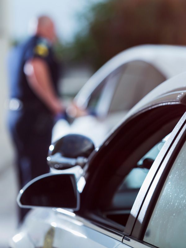 Close-up of a silver car at a roadside stop with a blurred police officer in the background