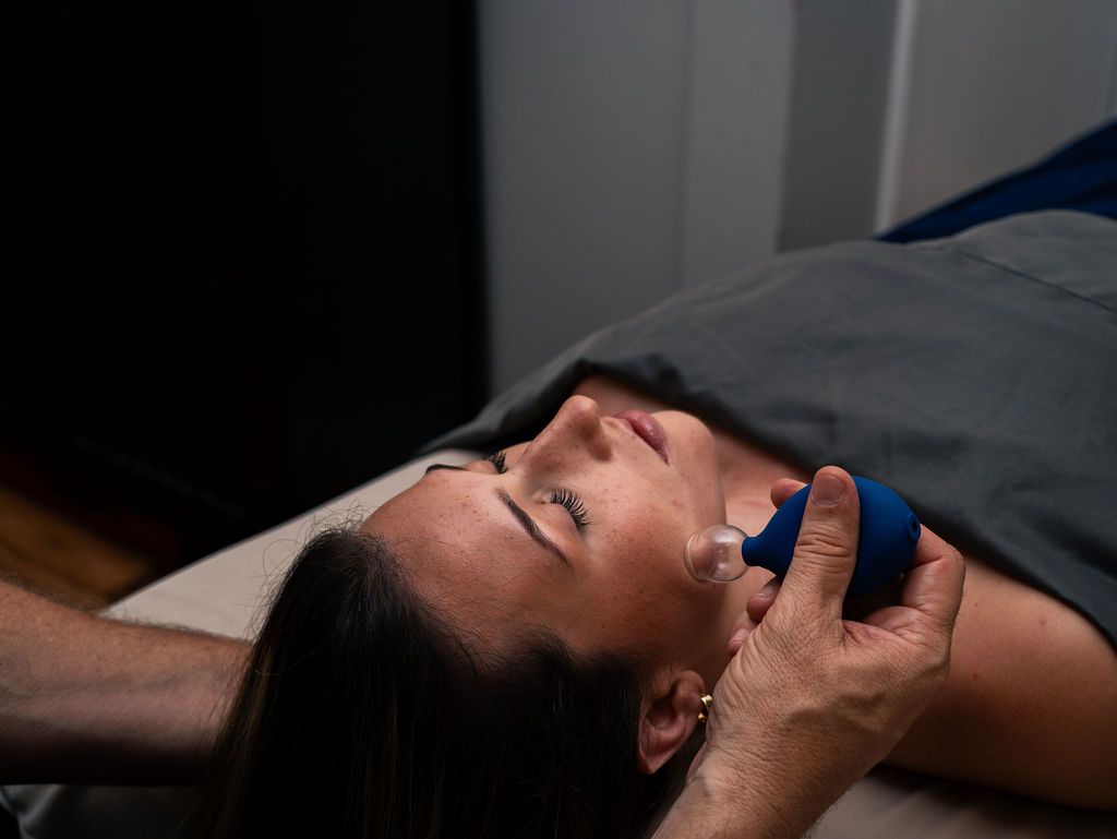 Woman lying on a bed with her face near a blue object, while another hand holds her head.