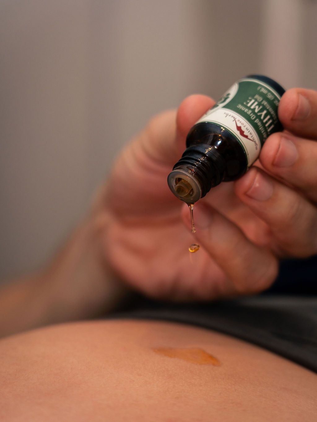 Hand holding a dropper bottle over a bare back with a droplet falling onto skin