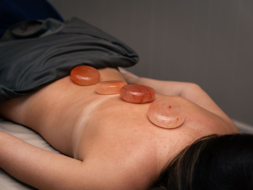 Person lying face down with hot stones placed on their bare back during a massage treatment