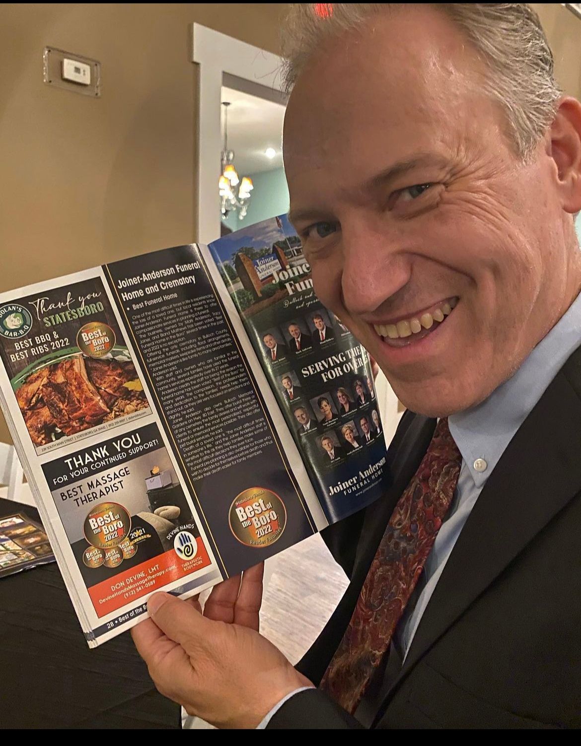 Smiling man in a suit holding open a brochure at an indoor event