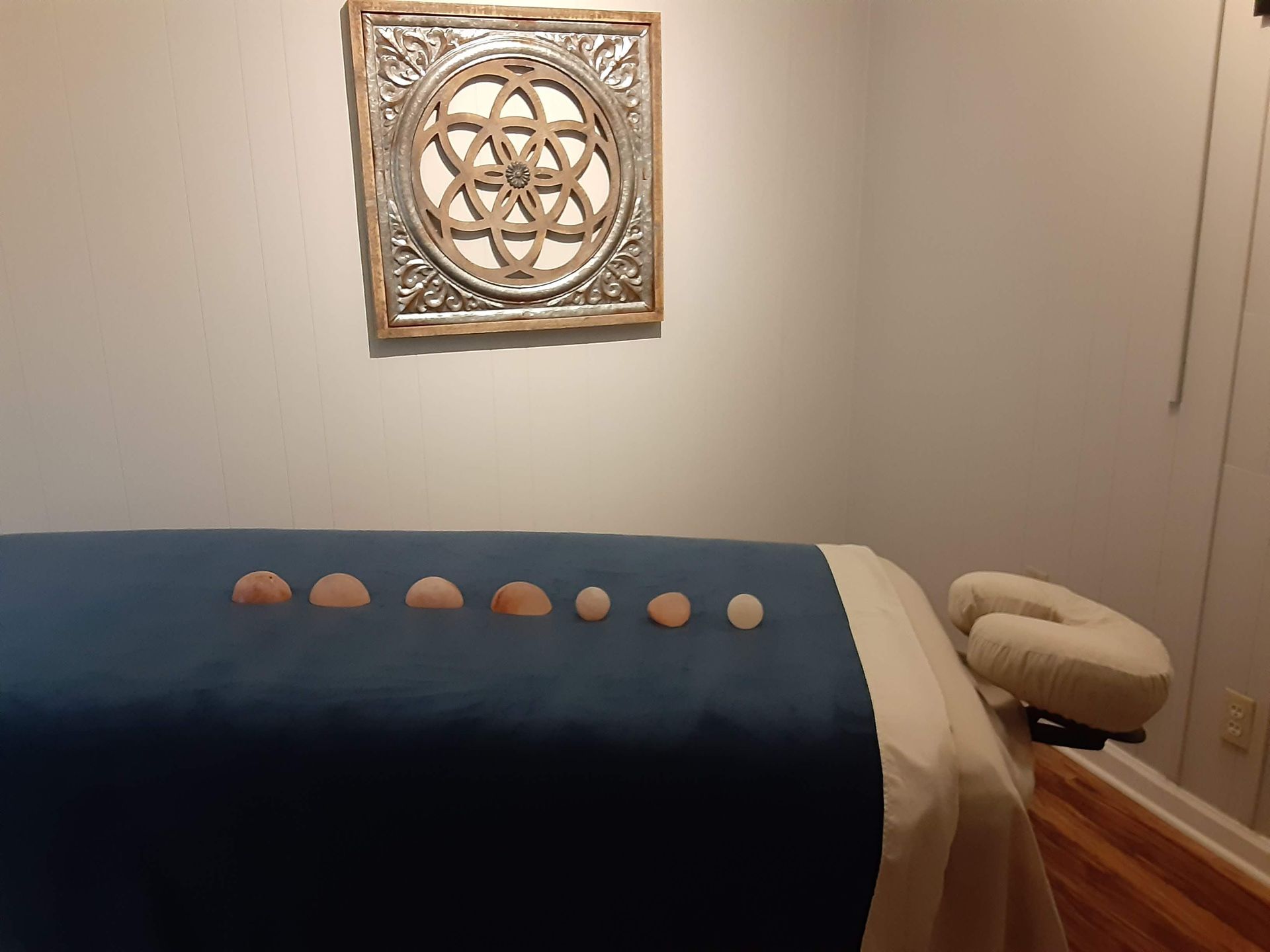 Massage table with blue cover in a spa room, wall art above and a small stool nearby