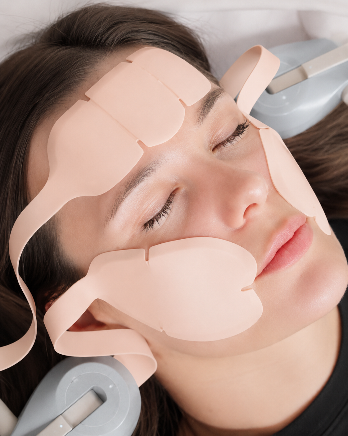 Person lying with facial adhesive patches on cheeks, forehead, and temples, eyes closed in a spa treatment.