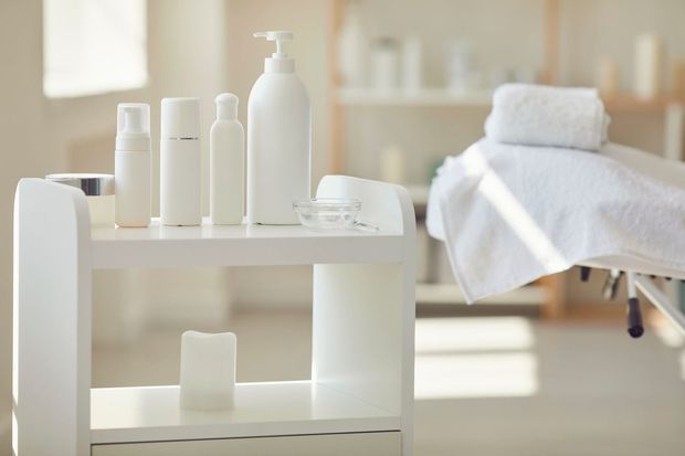 Spa treatment cart with white bottles and towels beside a massage table in a bright room
