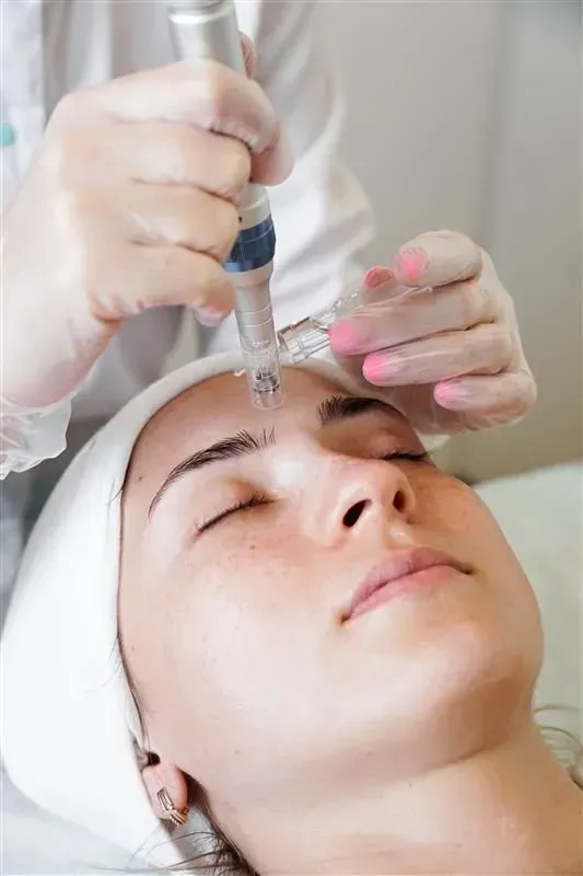 Cosmetician using a handheld device on a woman’s forehead during a facial treatment