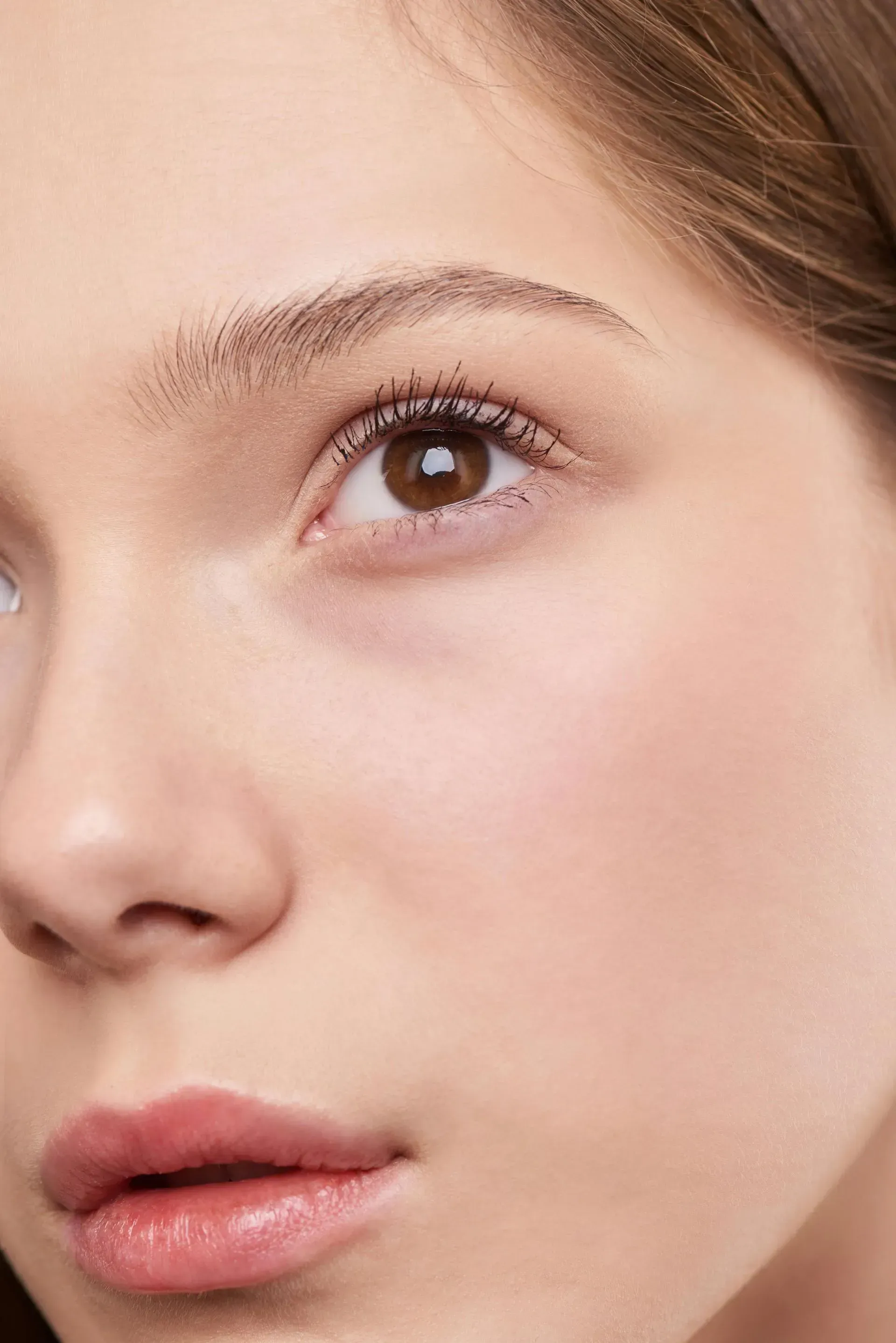 Close-up of a woman's face with soft makeup, looking upward against a light background