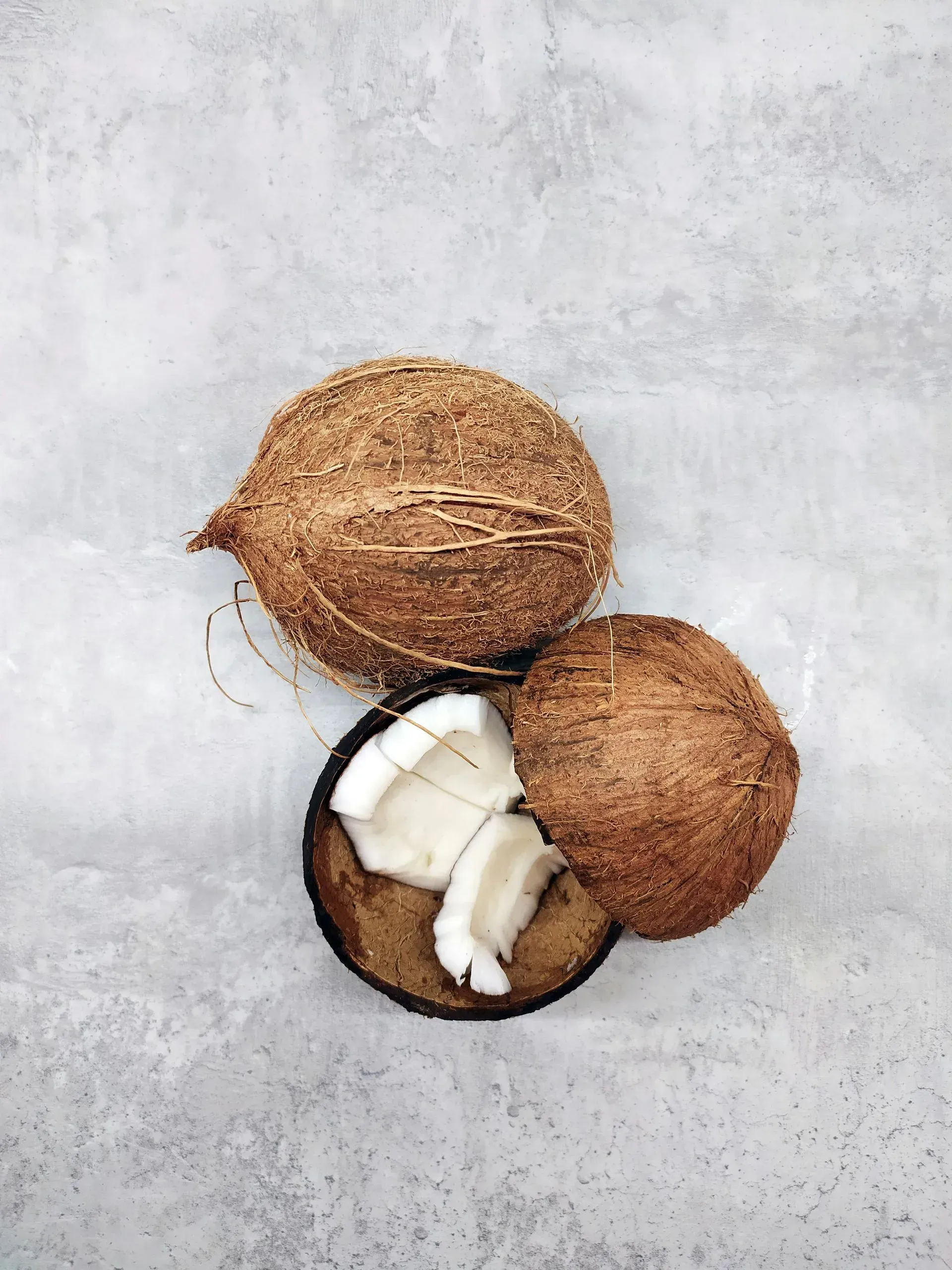 Three coconuts on a gray surface, one split open with white flesh visible