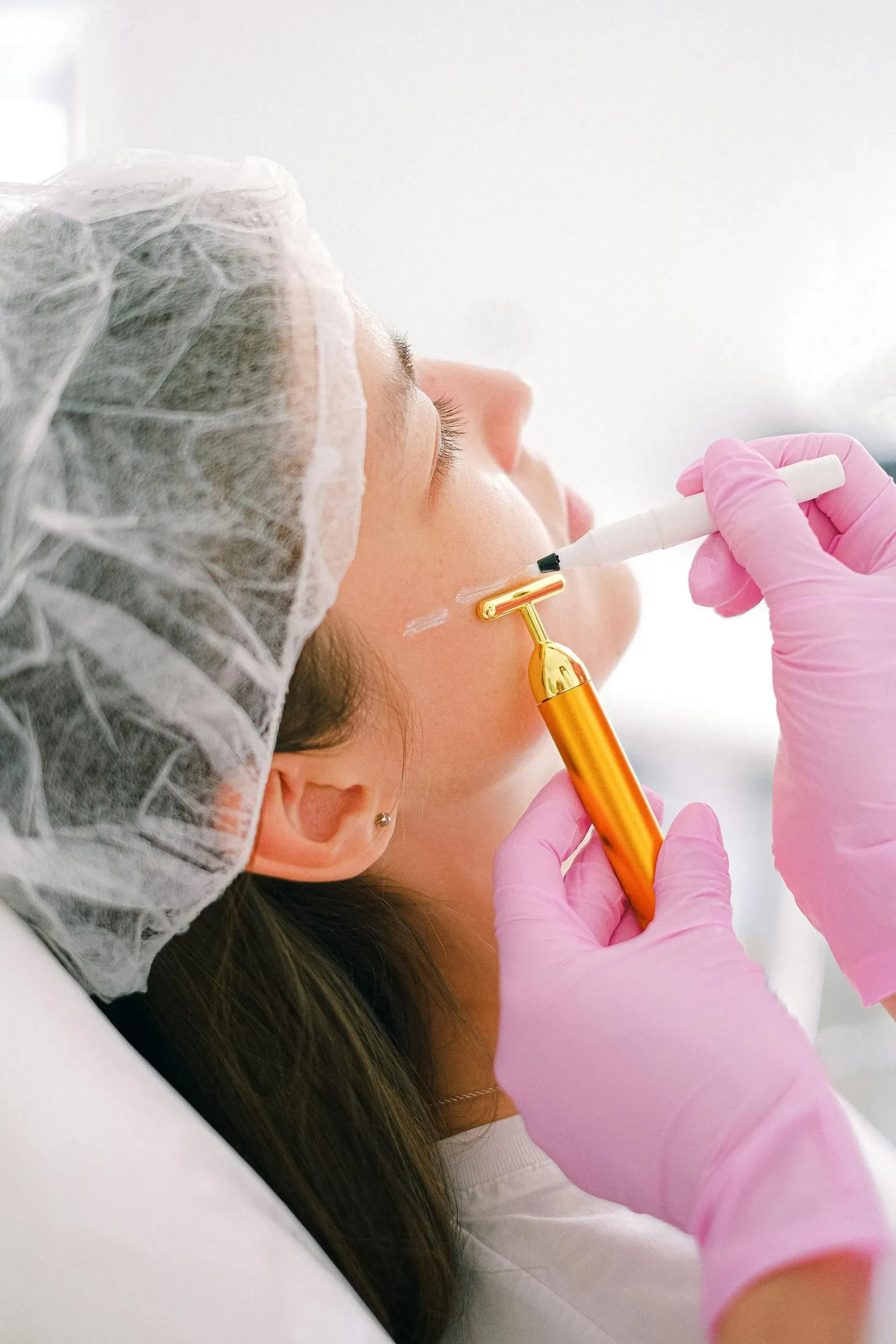 Cosmetic procedure on a woman’s face with gloved hands using a pen-like tool near her cheek