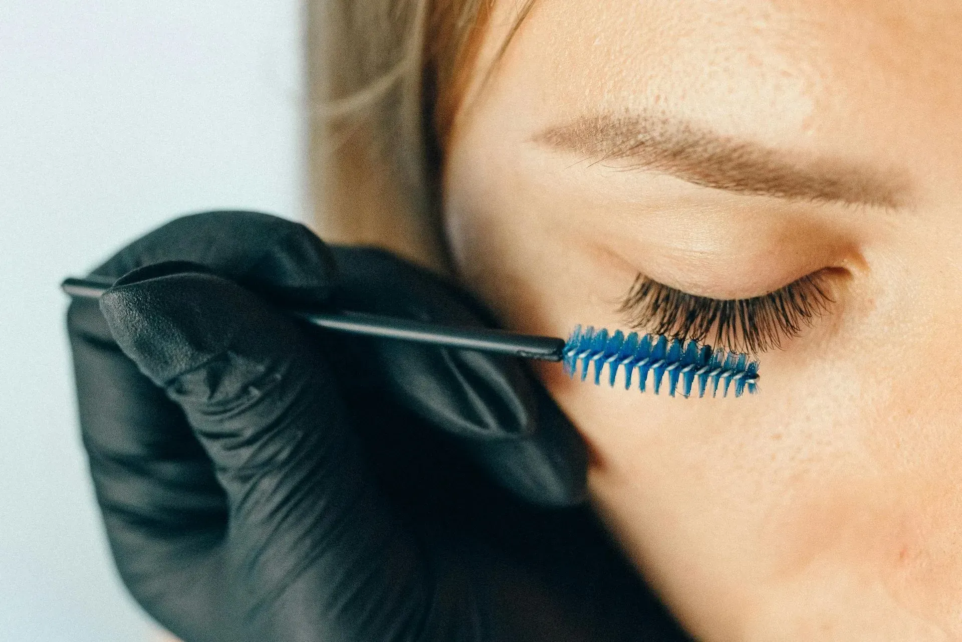 Gloved hand applying blue mascara to a closed eye