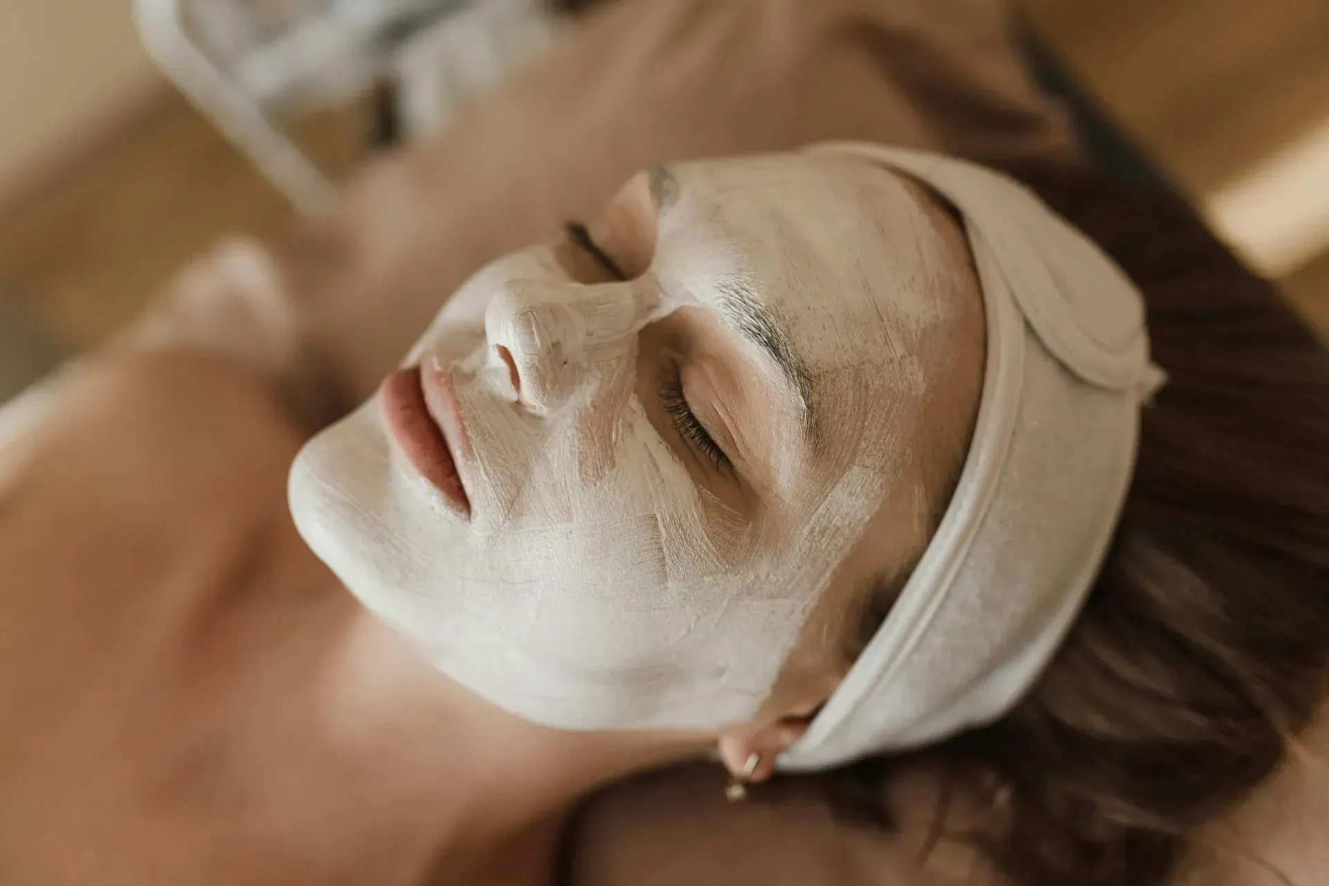 Person with a white facial mask and headband lying down during a spa treatment