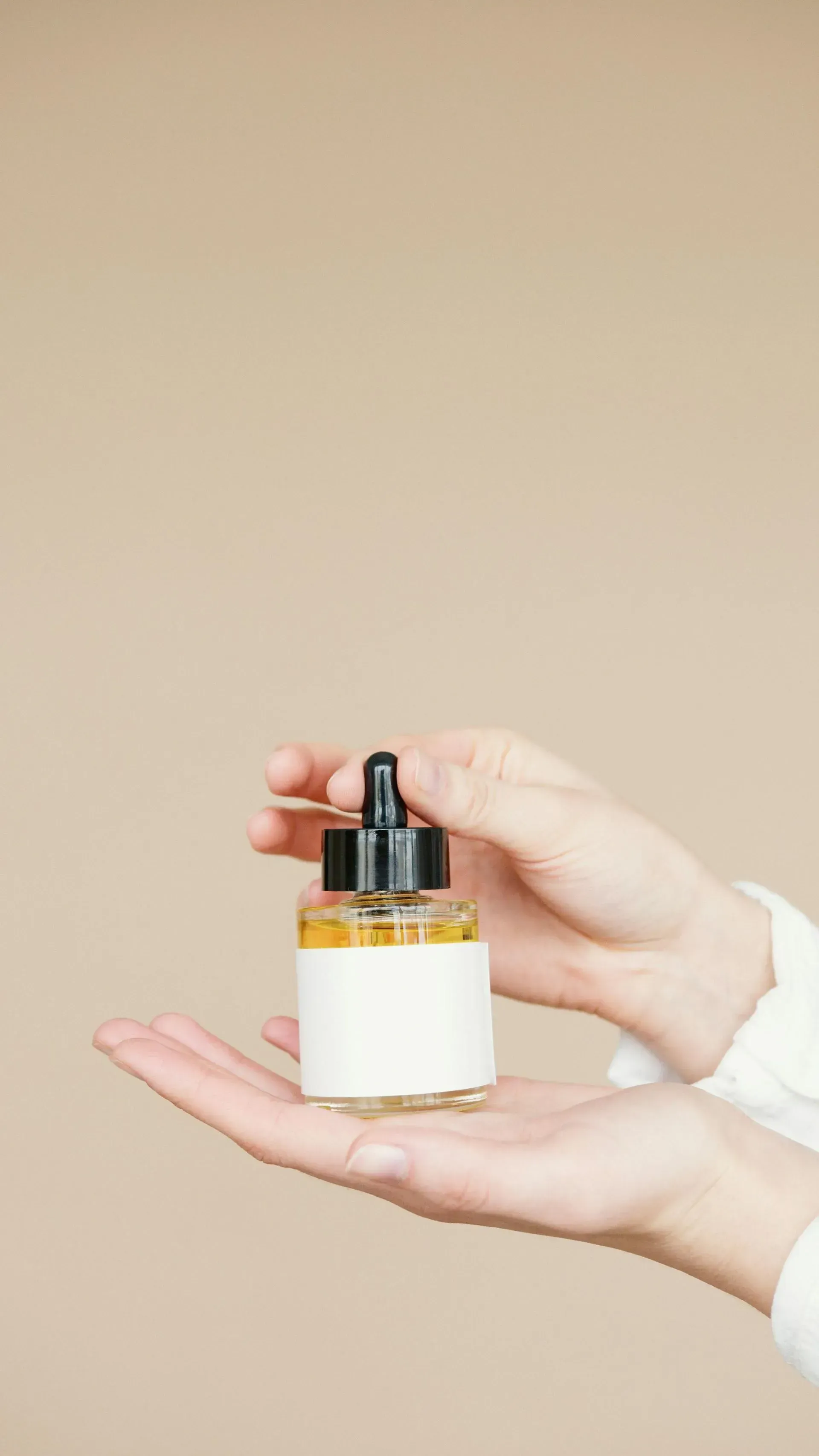 Hand holding a small amber dropper bottle with a white label against a beige background