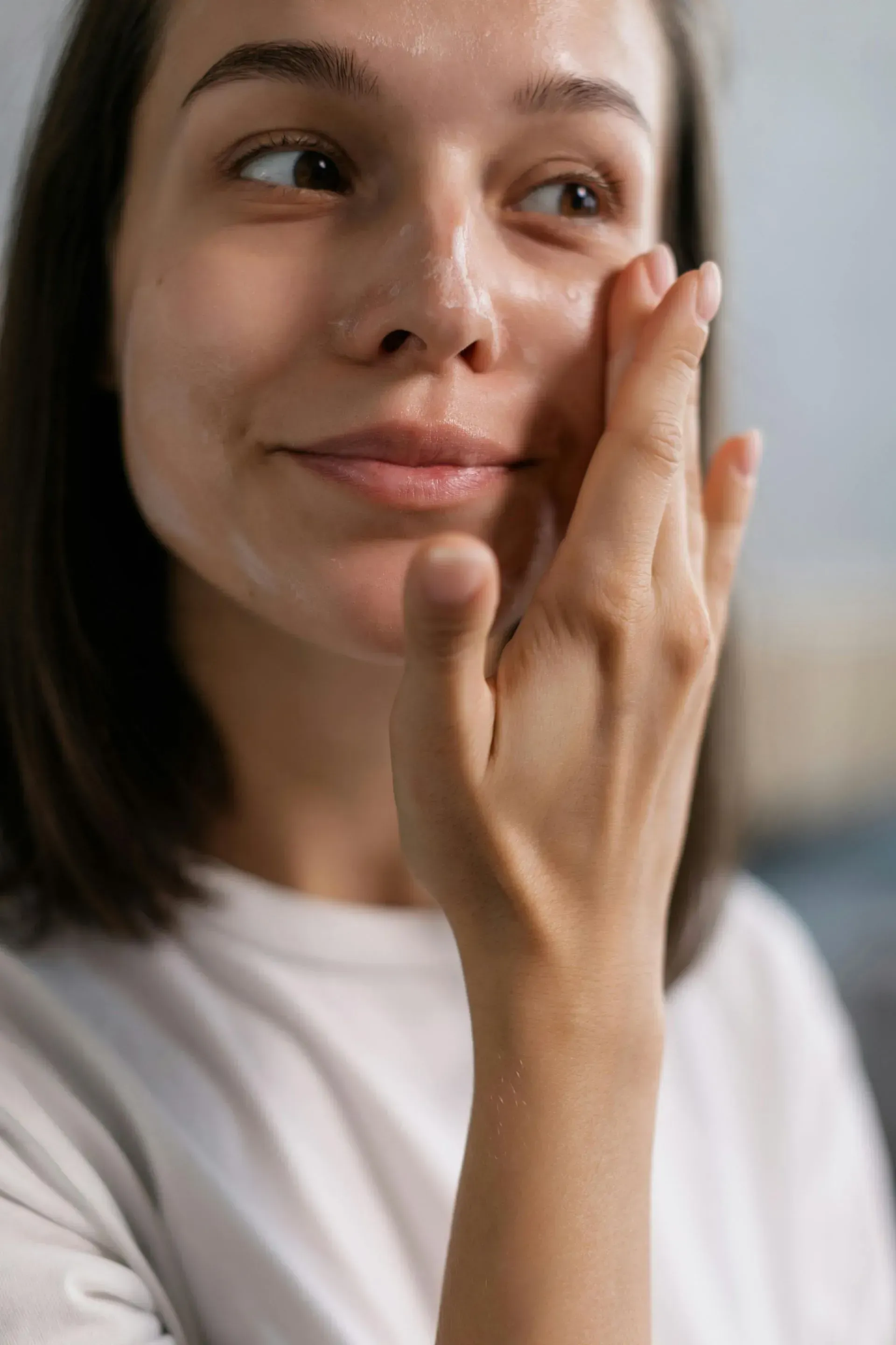 Woman applying skincare cream to her cheek in a softly lit indoor setting
