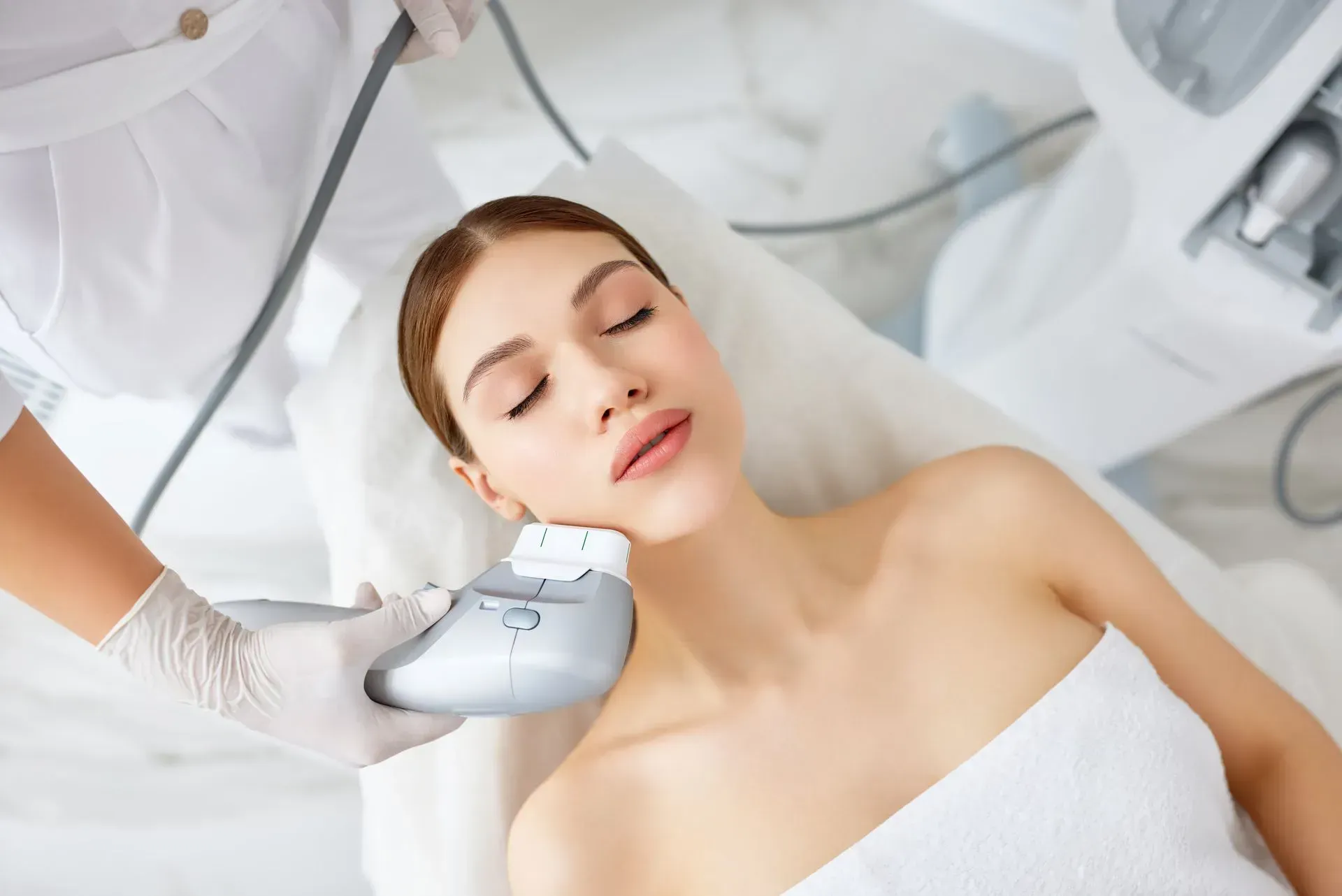 Woman receiving a facial treatment with a handheld device in a bright spa setting