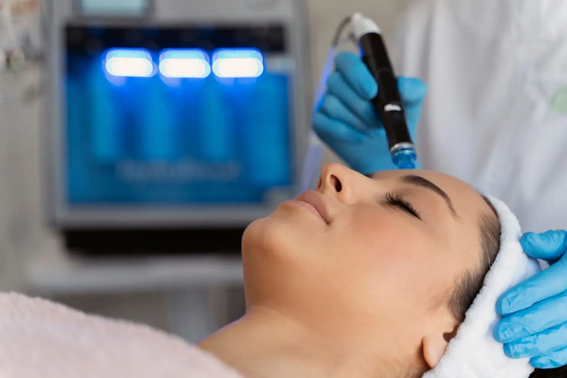 Facial treatment with blue-gloved esthetician using a handheld device on a woman’s forehead