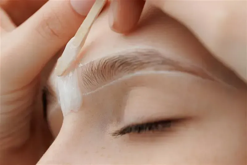 Cotton pad applying white cream to a closed eyebrow area