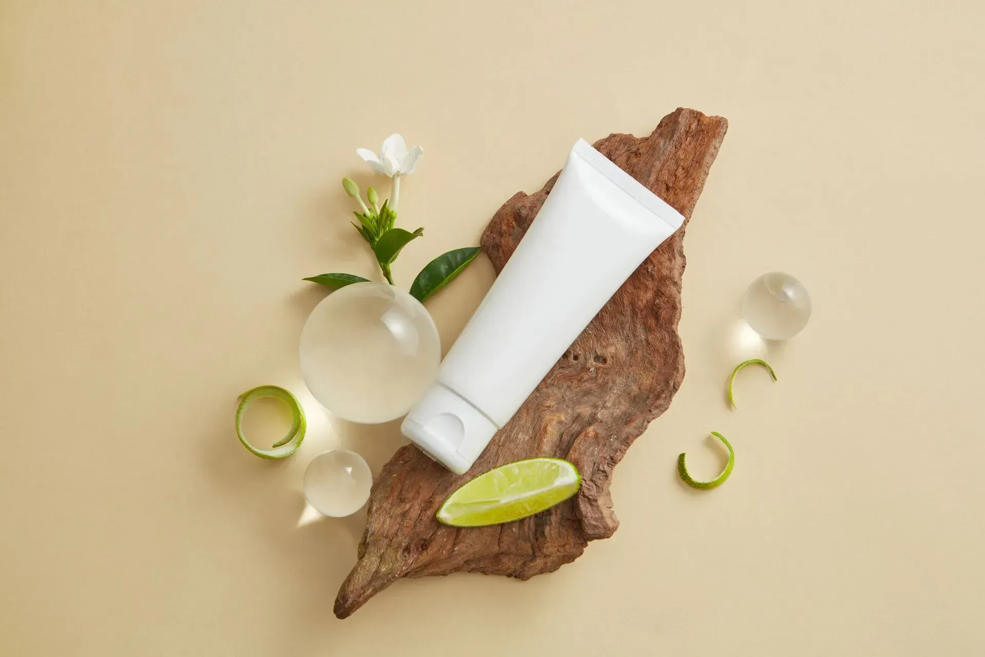 Skincare products and leaves arranged on a brown bark piece against a beige background