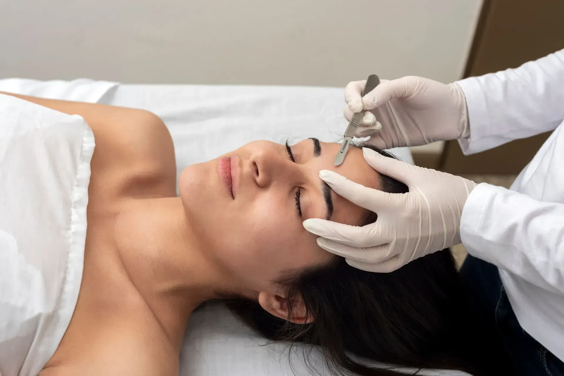 Cosmetic treatment on a woman’s face with gloved hands using a syringe near her forehead