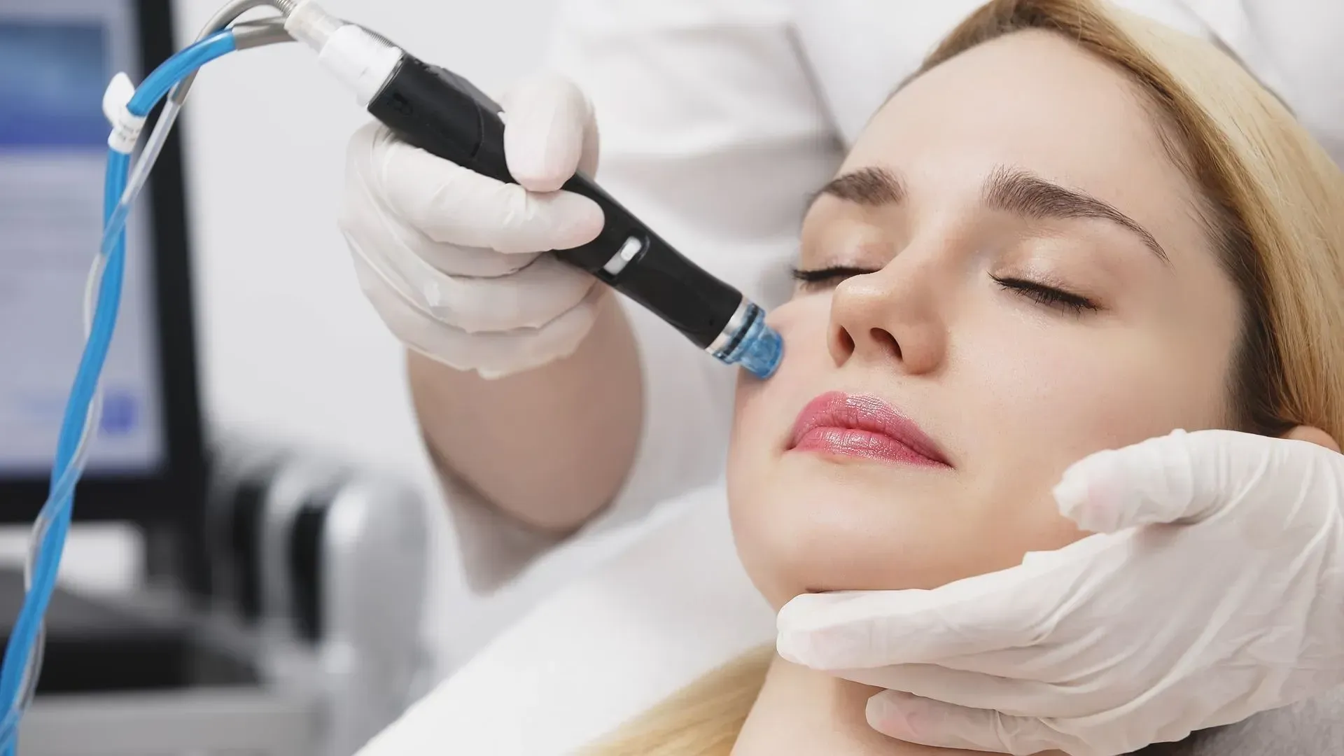 Esthetician using a handheld facial treatment device on a woman lying with eyes closed in a spa clinic
