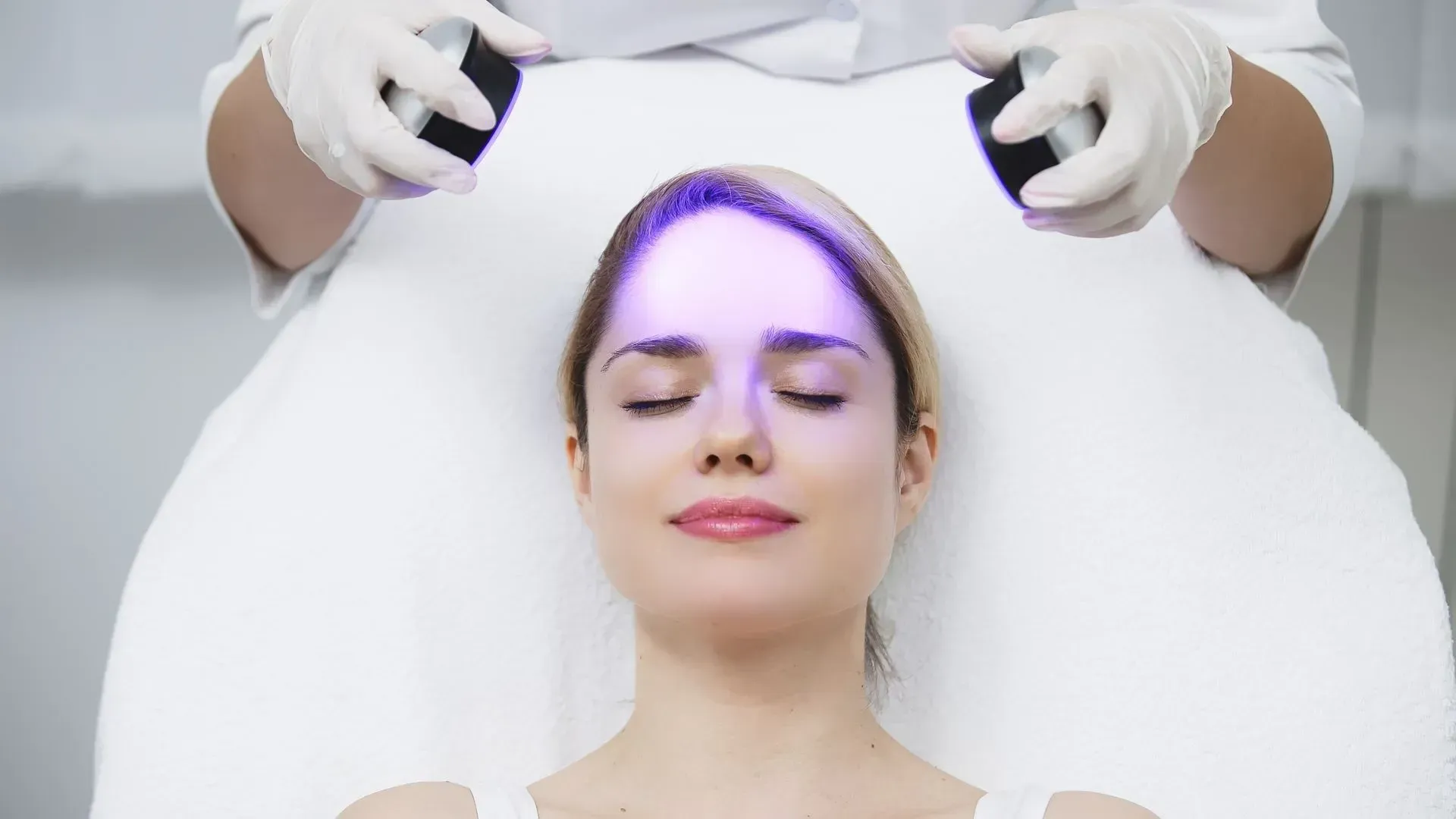 Woman receiving a purple light facial treatment with gloved hands in a spa setting