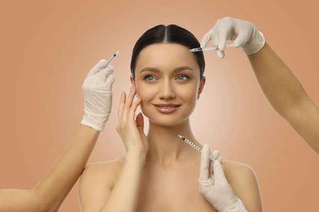 Woman receiving a facial treatment from gloved hands against a peach background