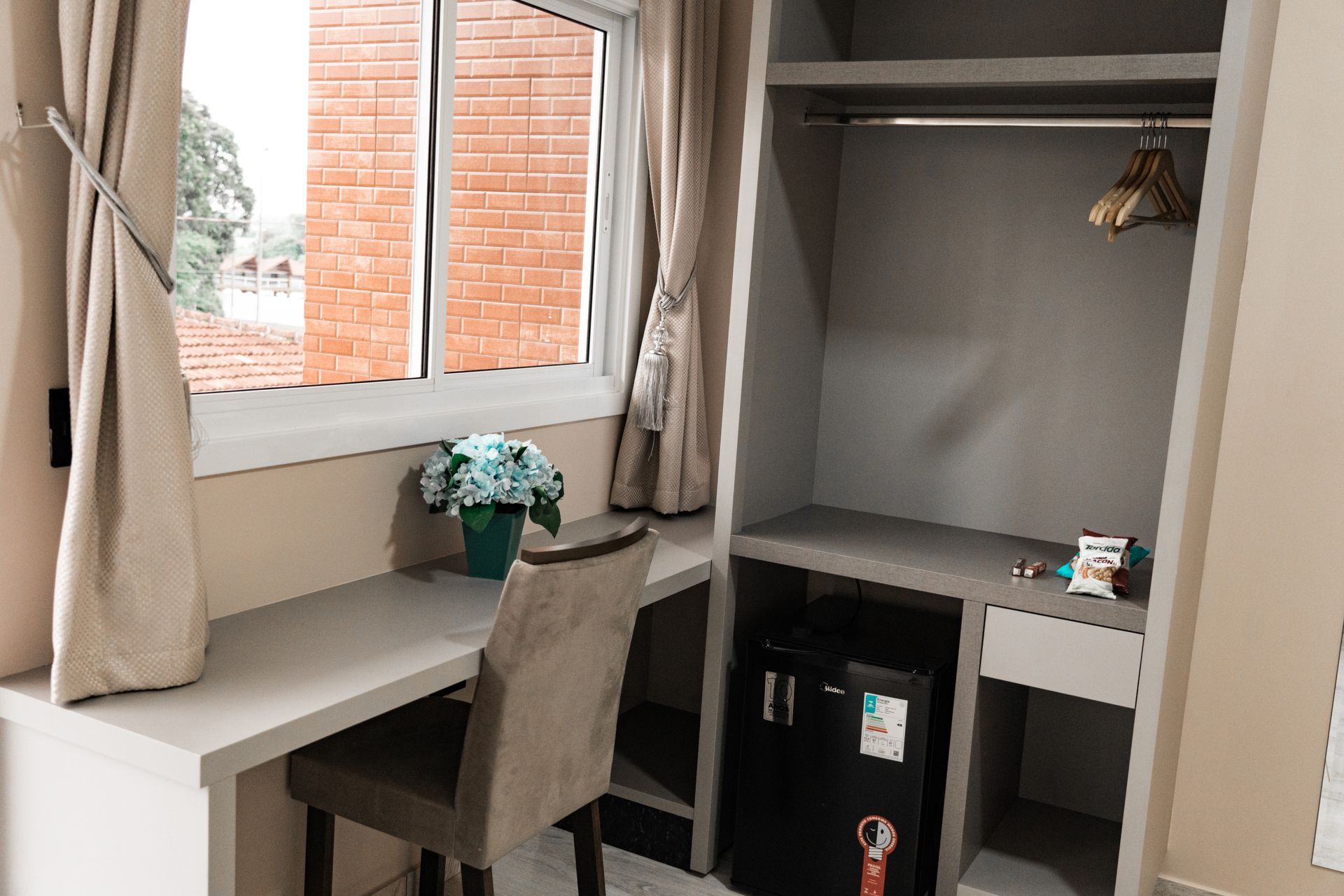 Um quarto de hotel com uma escrivaninha, cadeira, armário e janela. MD Recanto Hotel