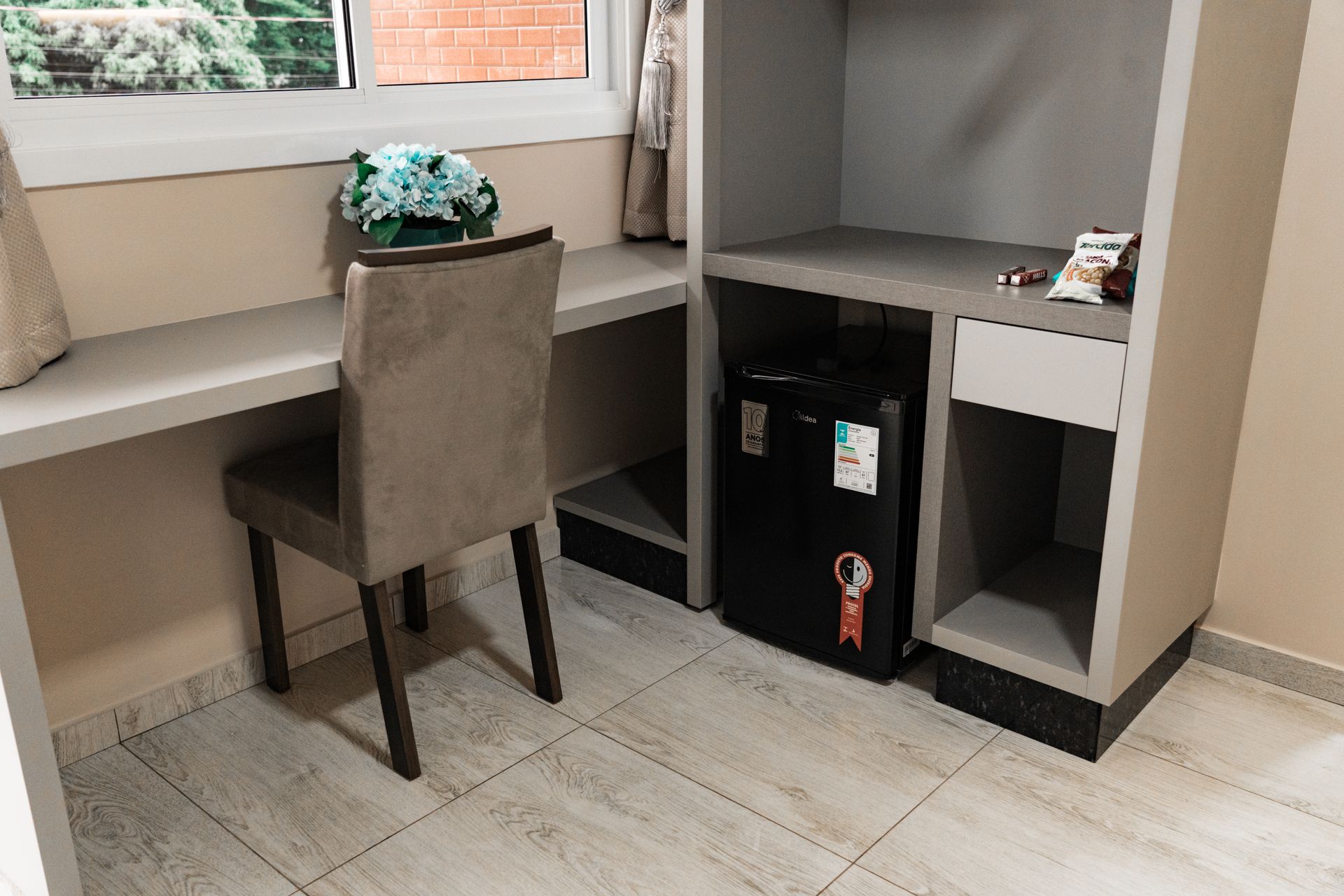 Um quarto com uma escrivaninha, cadeira, geladeira e uma janela. MD Recanto Hotel