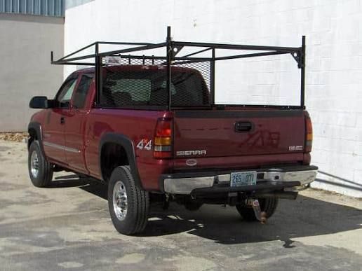 Red pickup truck with a black utility rack parked beside a white building.