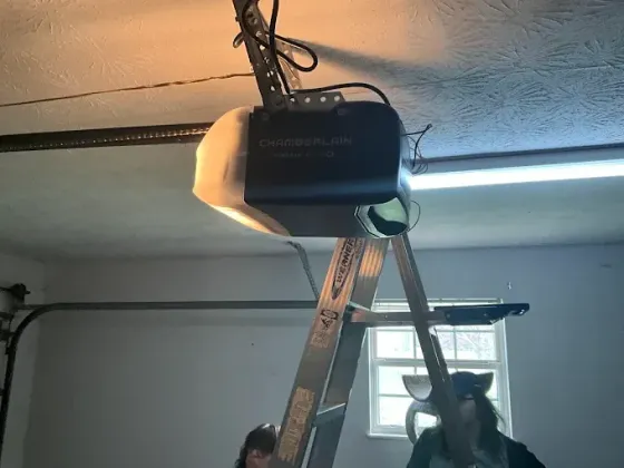 Garage ceiling with a ladder under a mounted black unit and fluorescent light; two people stand below.