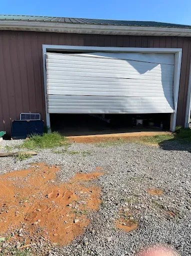 Partially open white garage door on a brown building with gravel driveway and dirt patch