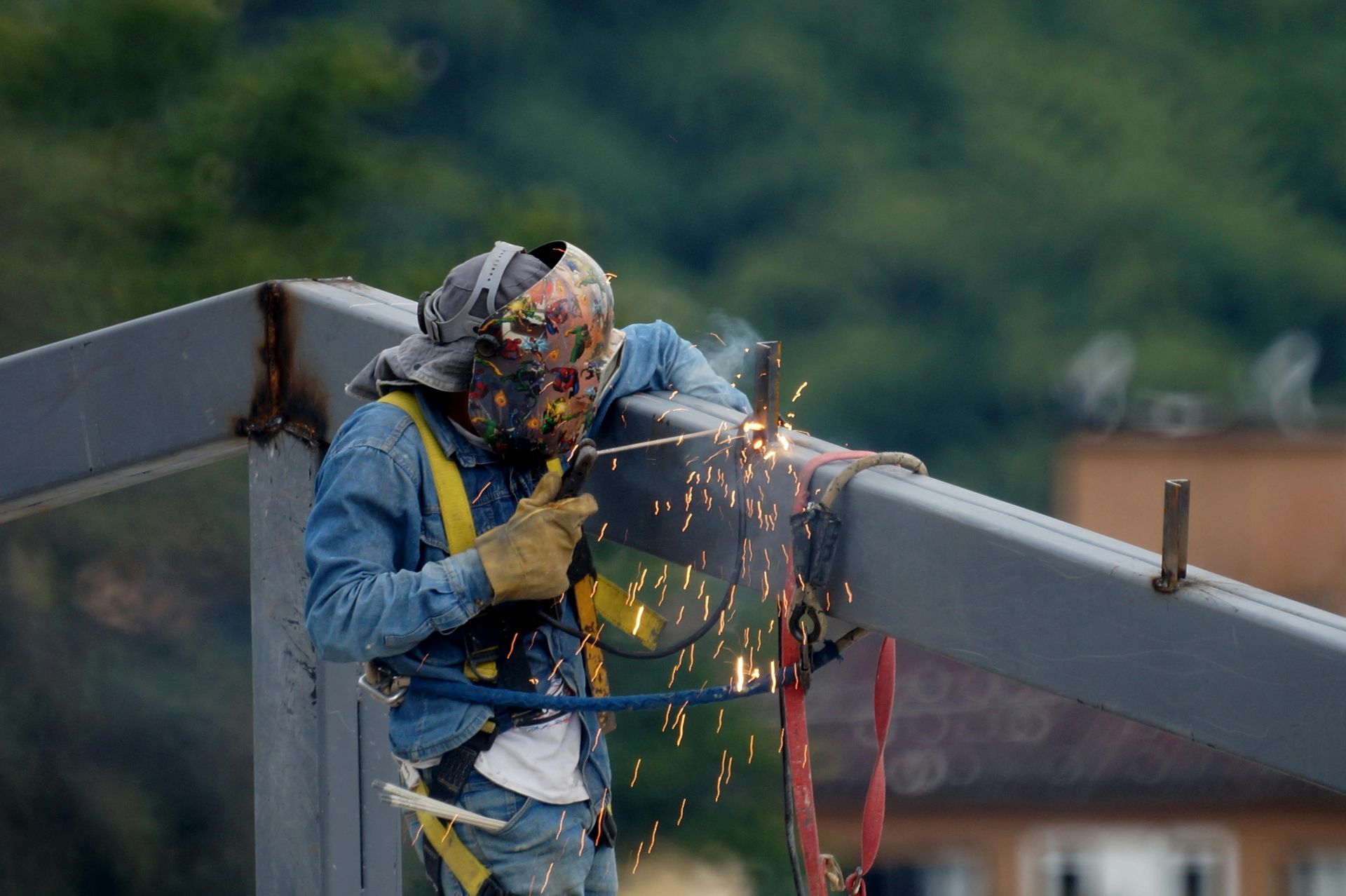 Worker welding steel beam on a bridge, sparks flying, wearing safety gear and harness