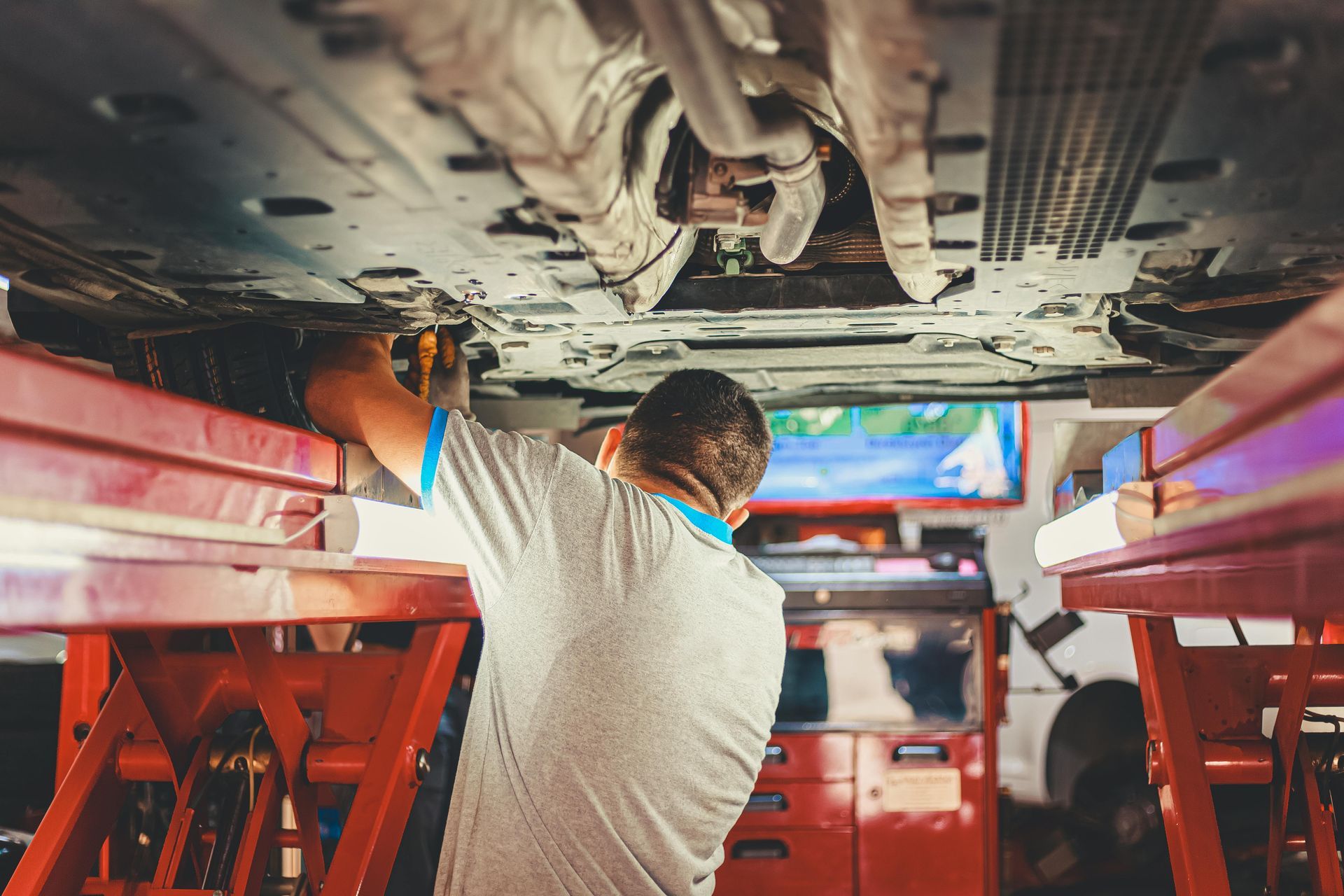 Worker repairing the underside of a vehicle in a red auto shop lift area