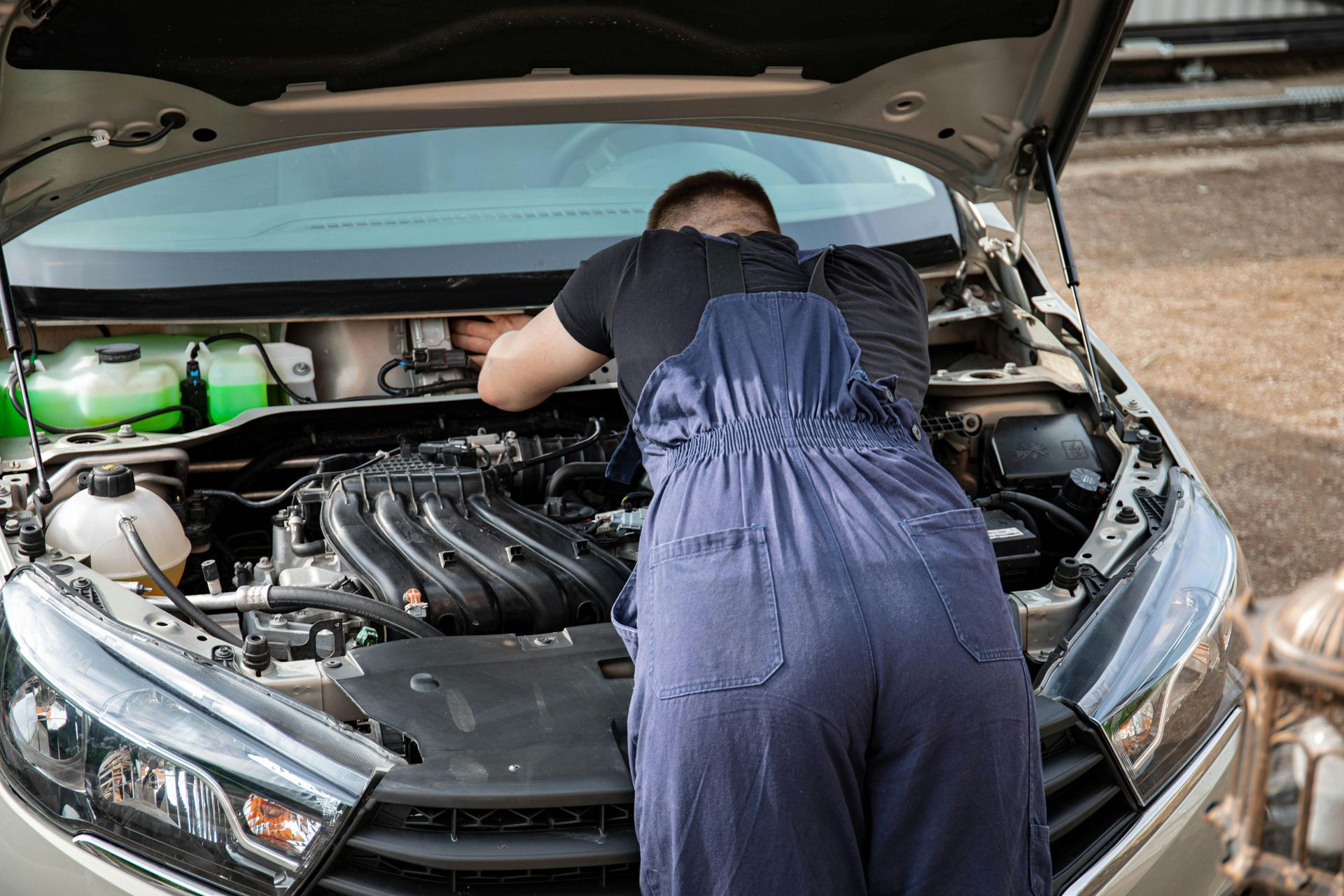Person leaning over an open car hood, inspecting the engine in a garage