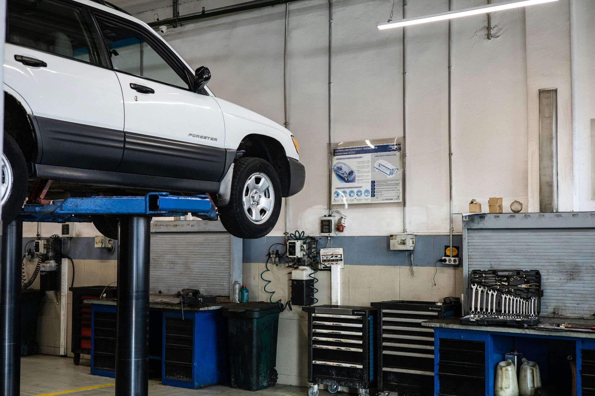 White SUV raised on a blue lift in an auto repair garage with tool carts and equipment