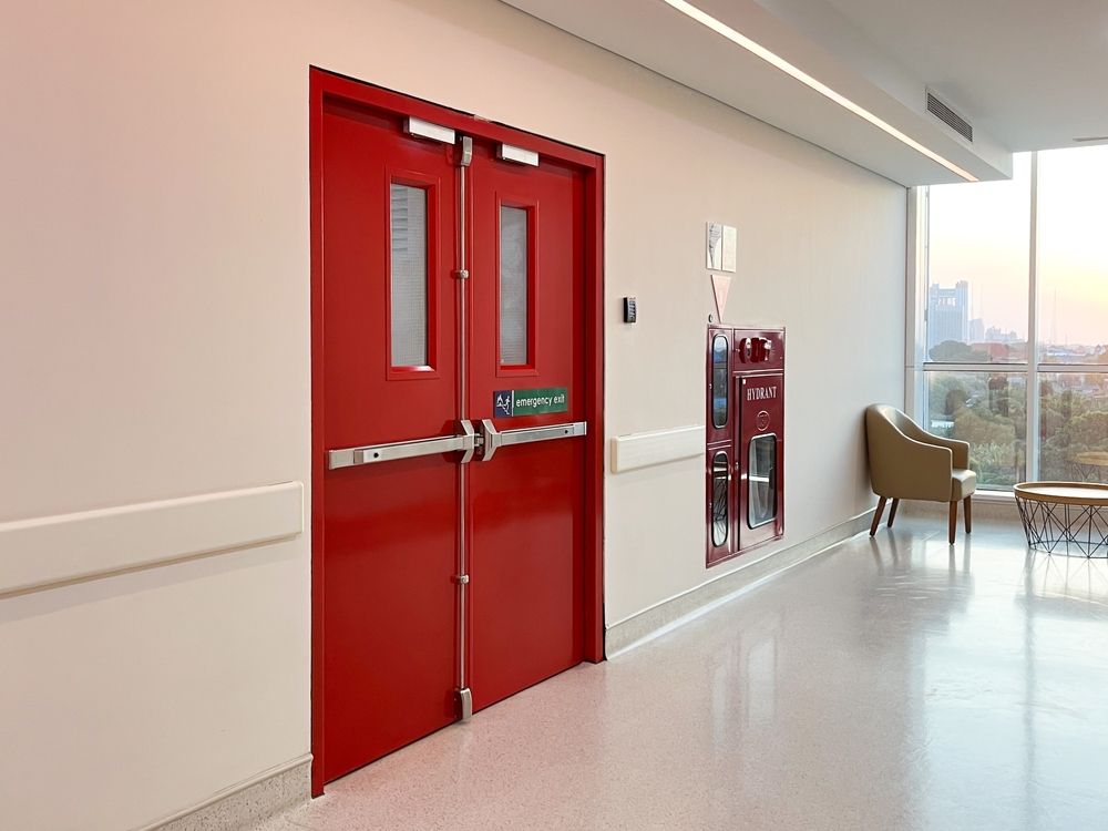 Red double doors in a bright hallway with a window and chairs nearby