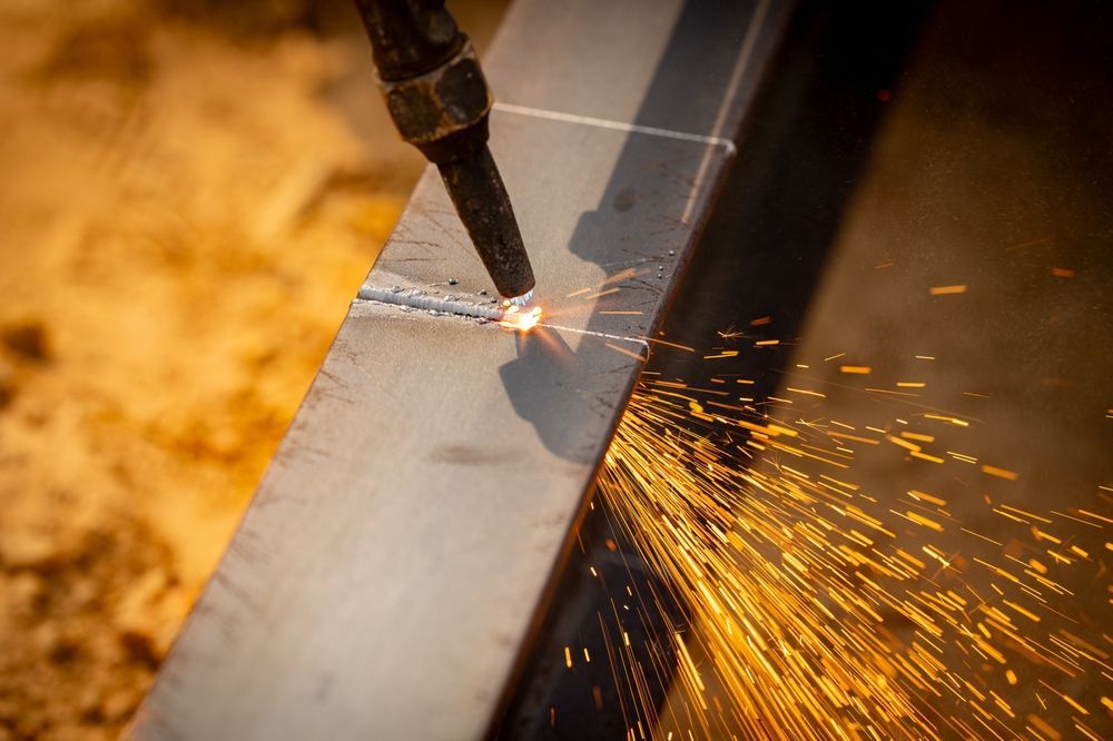 A cutting torch slices metal, sending bright orange sparks across a steel surface.