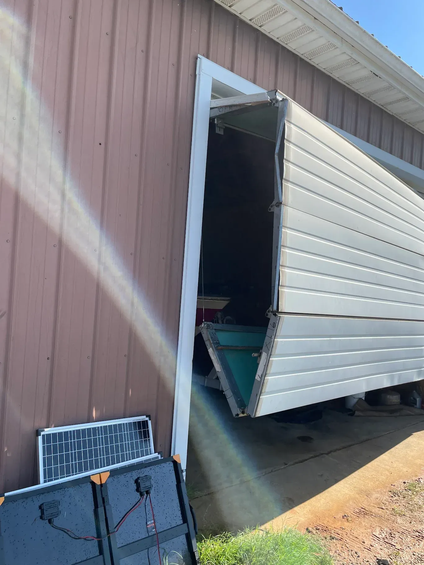Damaged garage door bent open on a pink building, exposing items inside.