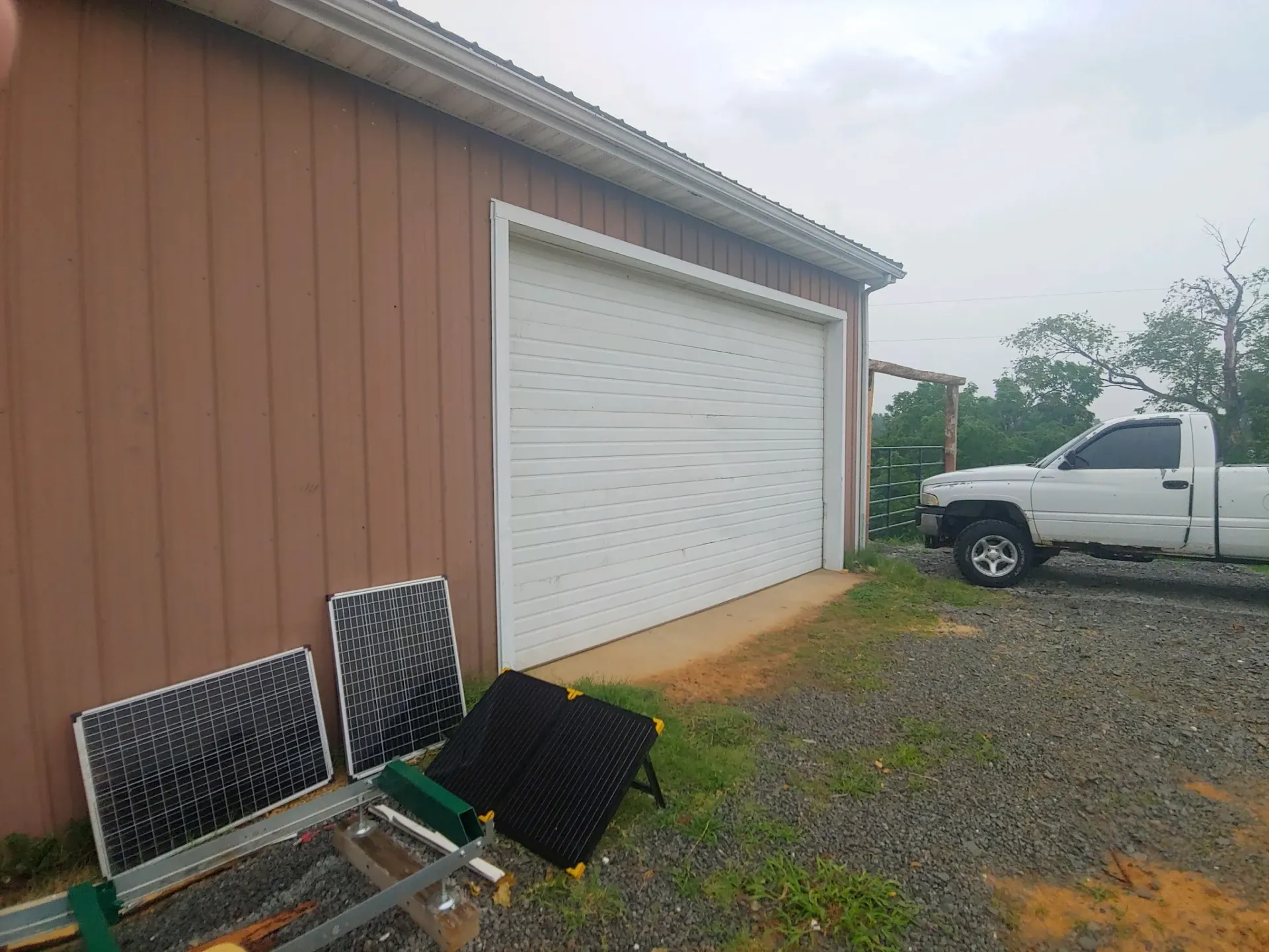 White garage door on a brown building with two chairs in gravel and a white truck parked beside it.