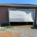 Partially open white garage door with a black car parked inside and gravel in front