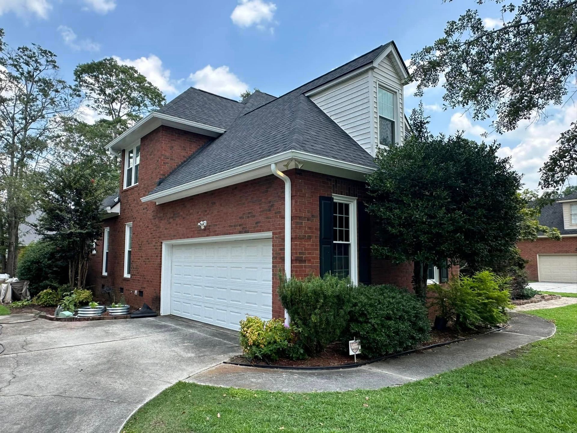 Brick two-story house with white garage, dark roof, and landscaped front yard in a suburban neighborhood