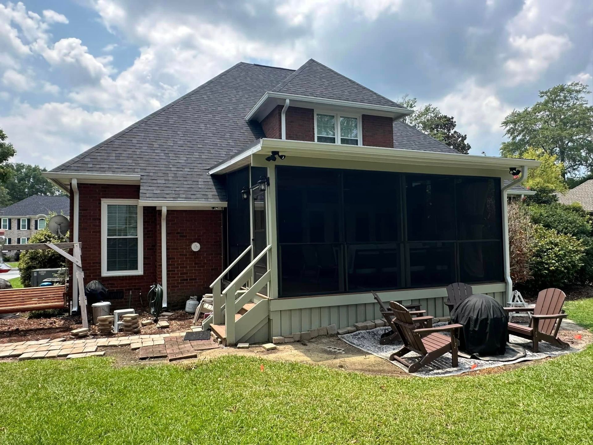Backyard house with screened porch, patio chairs, and stone fire pit under a cloudy sky