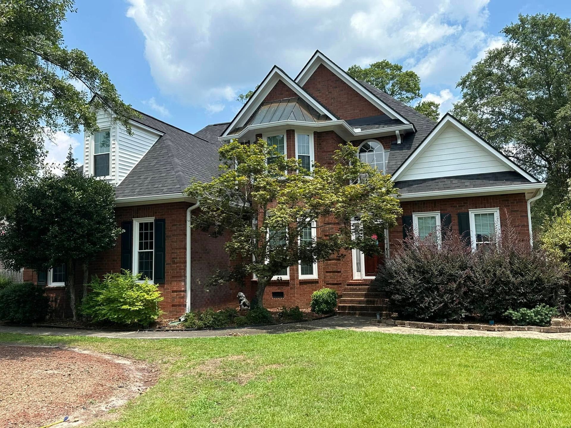 Brick house with peaked roof and front lawn under a partly cloudy sky
