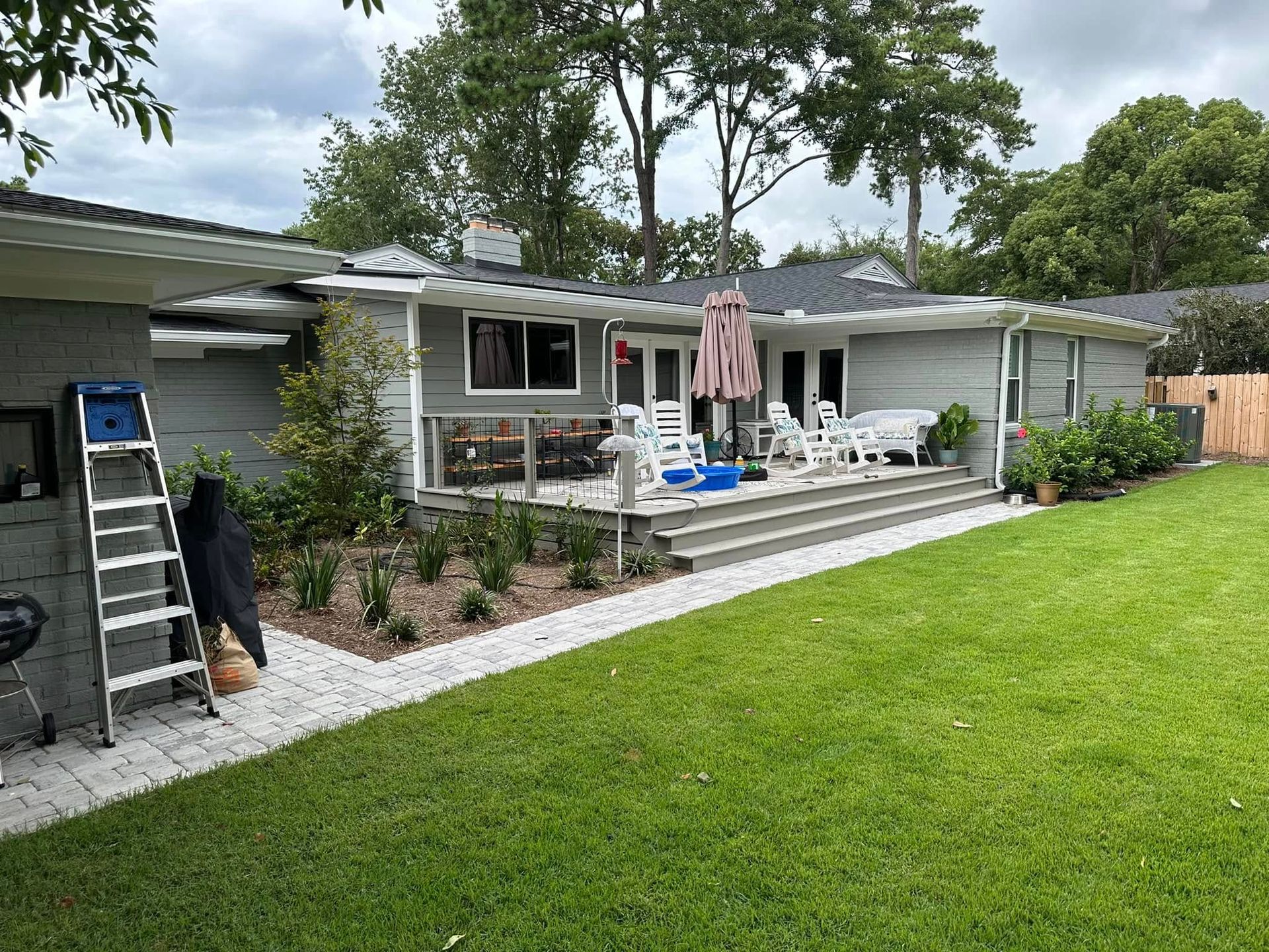 Single-story house with a front deck, patio chairs, umbrella, and a green lawn