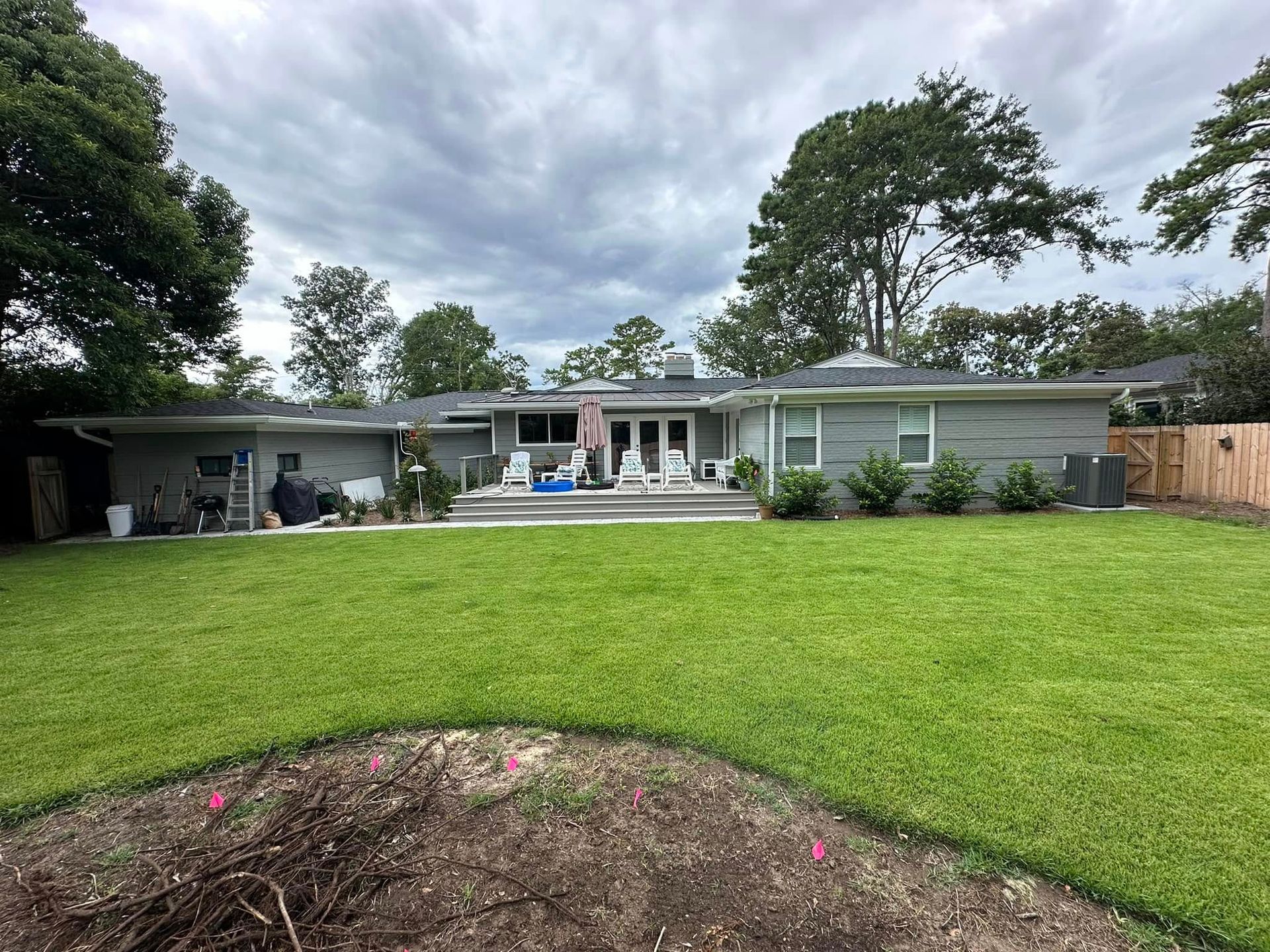 Single-story house with a wide green lawn, cloudy sky, and trees in the background