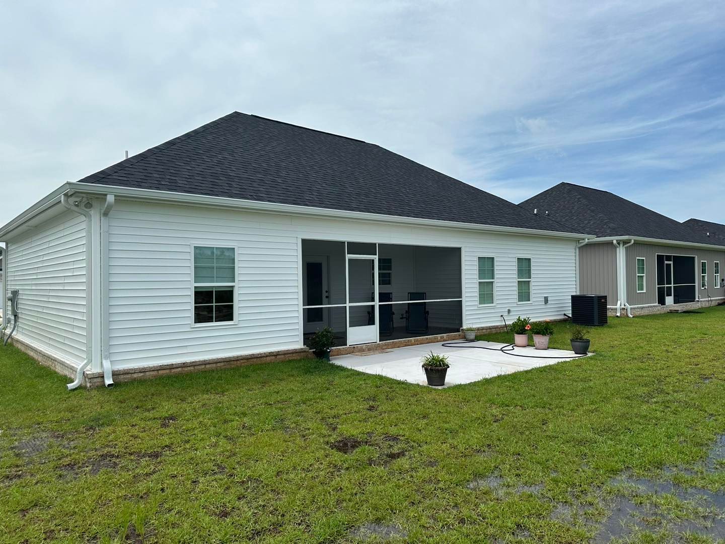Single-story white house with dark roof, screened porch, and a small front patio on a grassy lawn.