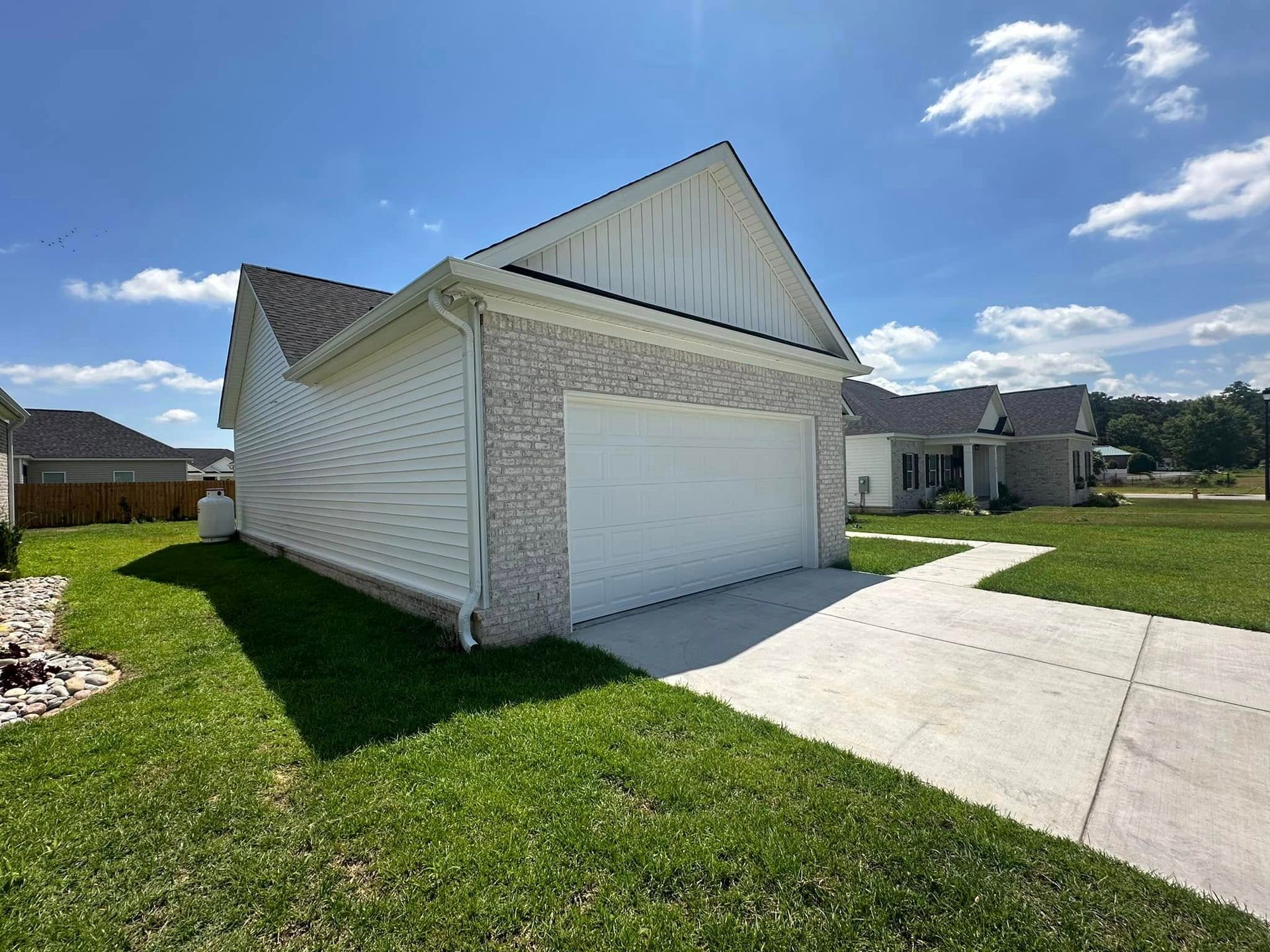 Suburban house with white siding and garage, front lawn, and driveway under a blue sky