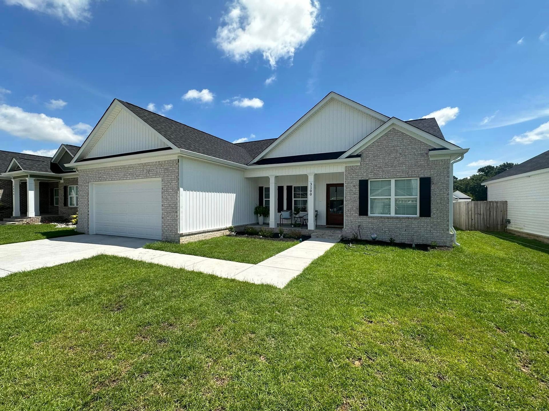 Single-story suburban house with white siding, stone accents, a garage, and a green lawn under a blue sky.