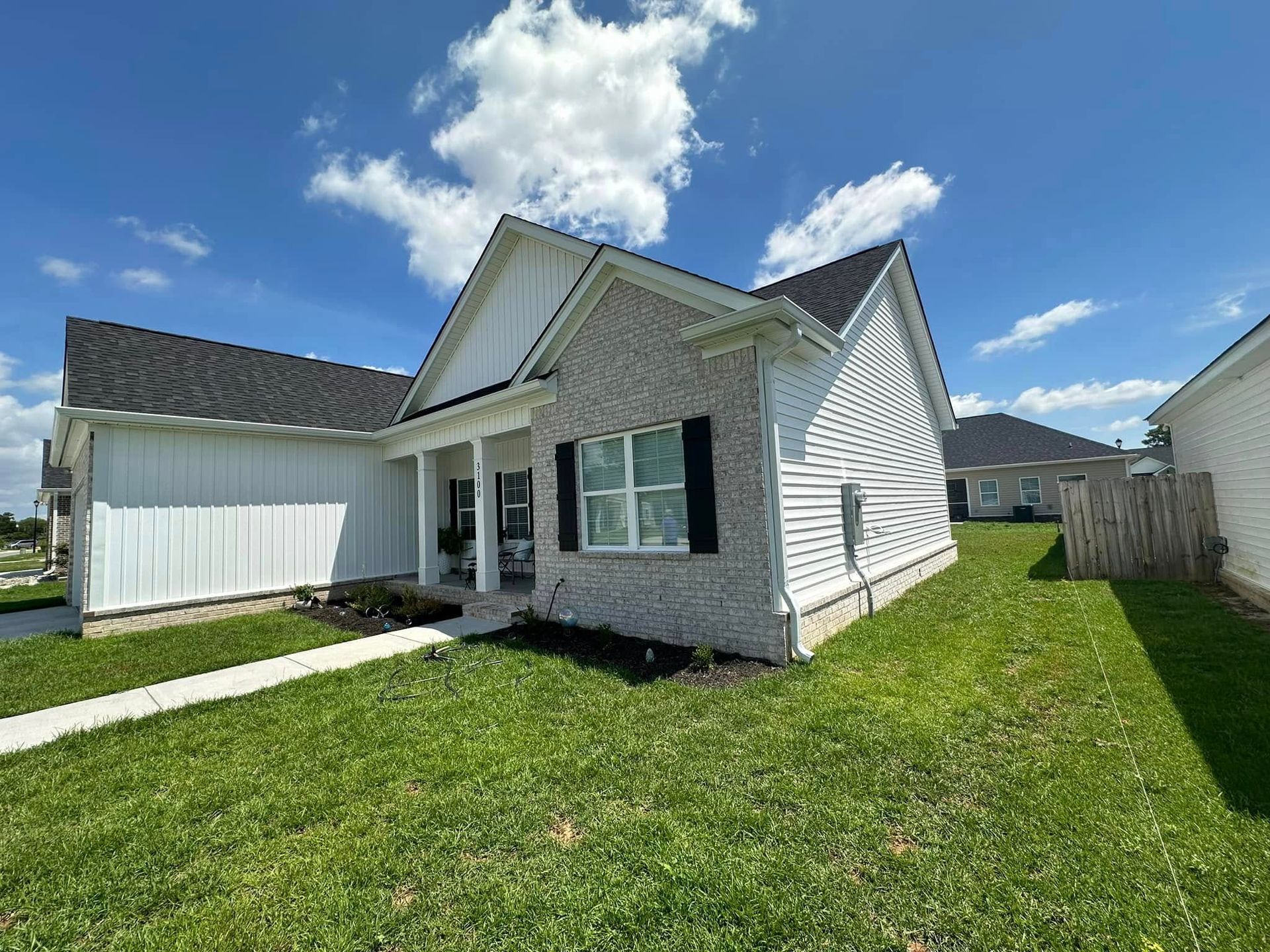 Suburban house with white siding, dark roof, and a green lawn under a blue sky